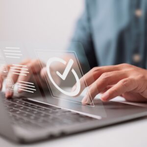 Man's hand on a laptop keyboard with a holographic checkmark symbol indicating successful online certification.