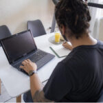 Man working on a laptop with a notepad on the side taking notes indicating successful personal brand requires extensive research