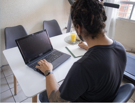 Man working on a laptop with a notepad on the side taking notes indicating successful personal brand requires extensive research